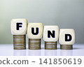 Fund icon in wooden block on stack coins with a rising stock market chart in the background, symbolizing financial growth and successful investments. 141850619