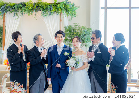 A family photo of the bride and groom and their parents standing side by side at the wedding reception venue. A family photo of the bride and groom and their parents standing side by side at the wedding reception venue. 141852624