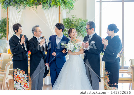 婚禮宴會廳裡,新郎新娘和他們的父母並肩站在一起,這是一張全家福照片。 婚禮宴會廳裡,新郎新娘和他們的父母並肩站在一起,這是一張全家福照片。 141852626
