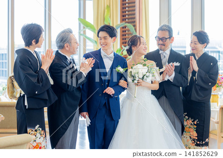 A family photo of the bride and groom and their parents standing side by side at the wedding reception venue. A family photo of the bride and groom and their parents standing side by side at the wedding reception venue. 141852629