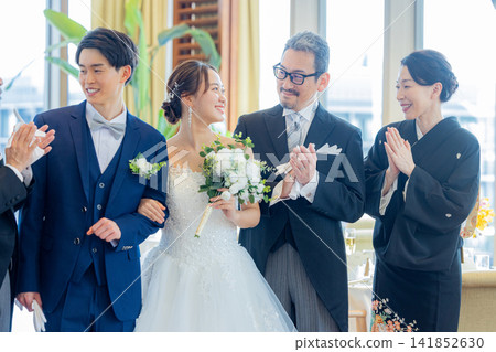 A family photo of the bride and groom and their parents standing side by side at the wedding reception venue. A family photo of the bride and groom and their parents standing side by side at the wedding reception venue. 141852630