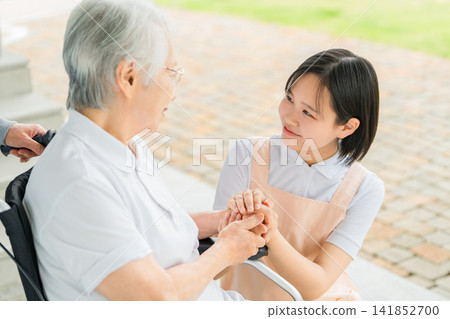 坐在輪椅上的老人和護理人員(助手/物理治療師)在醫院/護理設施中邊走邊說話 坐在輪椅上的老人和護理人員(助手/物理治療師)在醫院/護理設施中邊走邊說話 141852700