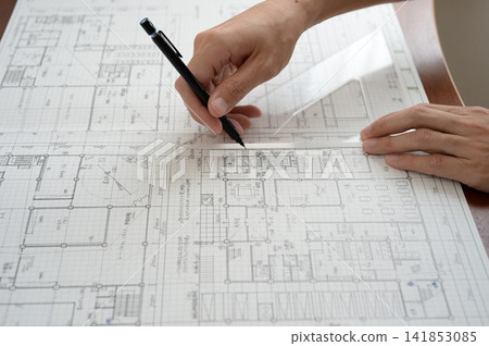 An architect's hands drawing lines on architectural drawings using a ruler and pen. An architect's hands drawing lines on architectural drawings using a ruler and pen. 141853085