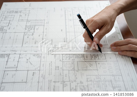 An architect's hands drawing lines on architectural drawings using a ruler and pen. An architect's hands drawing lines on architectural drawings using a ruler and pen. 141853086