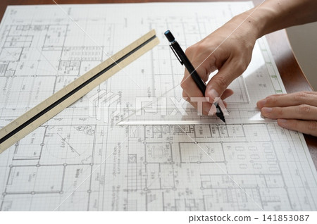 An architect's hands drawing lines on architectural drawings using a ruler and pen. An architect's hands drawing lines on architectural drawings using a ruler and pen. 141853087
