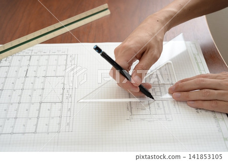 An architect's hands drawing lines on architectural drawings using a ruler and pen. An architect's hands drawing lines on architectural drawings using a ruler and pen. 141853105
