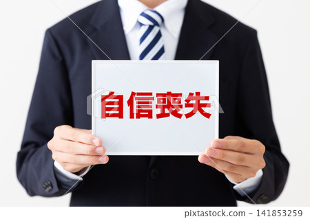 A young businessman in a business suit holding a whiteboard, looking dejected. A young businessman in a business suit holding a whiteboard, looking dejected. 141853259