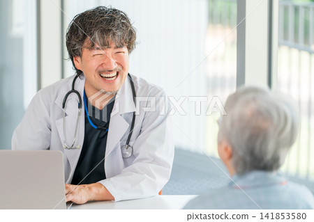 A male doctor in a white coat examines an elderly female patient. 141853580