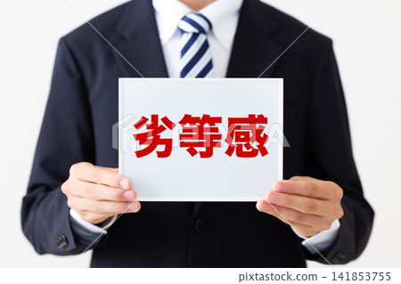 A young businessman in a business suit holding a whiteboard of feelings of inferiority. A young businessman in a business suit holding a whiteboard of feelings of inferiority. 141853755
