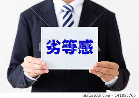 一位身穿西裝的年輕商人,手裡拿著一塊寫滿自卑感的白板。 一位身穿西裝的年輕商人,手裡拿著一塊寫滿自卑感的白板。 141853766