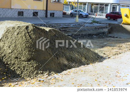 Construction work takes place on city street with dirt piles equipment Construction work takes place on city street with dirt piles equipment 141853974