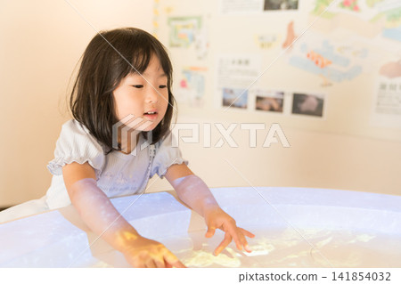 A young Japanese girl touches a light-up interactive display stand in a museum. A young Japanese girl touches a light-up interactive display stand in a museum. 141854032