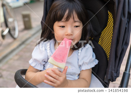 A Japanese toddler girl sitting in a stroller and munching on watermelon. A Japanese toddler girl sitting in a stroller and munching on watermelon. 141854198