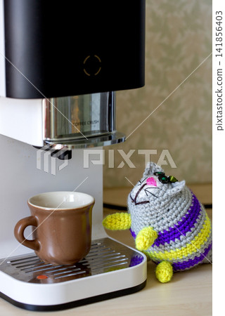 A knitted cat stands on a coffee machine. A knitted cat stands on a coffee machine. 141856403