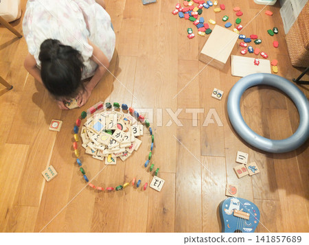 A girl in a dress is in a room cluttered with toys. A girl in a dress is in a room cluttered with toys. 141857689