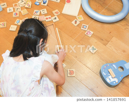 A girl in a dress is in a room cluttered with toys. A girl in a dress is in a room cluttered with toys. 141857691