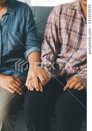 Supportive caregiver places hand over female client's hands during counseling on sofa, showing reassurance, empathy, mental health care, emotional support, trust, comfort, and healing indoors. Supportive caregiver places hand over female client's hands during counseling on sofa, showing reassurance, empathy, mental health care, emotional support, trust, comfort, and healing indoors. 141858035
