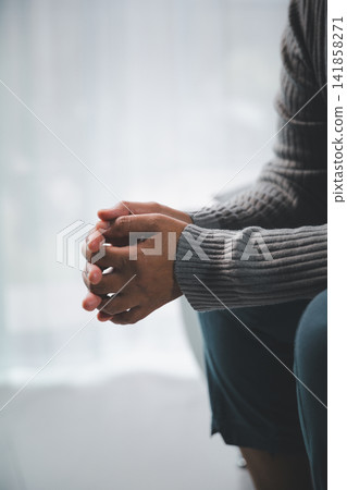 Close-up side view of an adult sitting with clasped hands, expressing anxiety, stress, uncertainty, or quiet contemplation, with generous copy space for mental health concepts. 141858271
