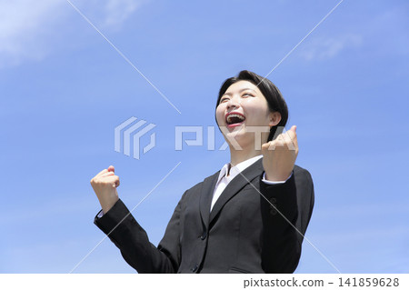 一位女上班族從低角度做出勝利的手勢,象徵成長和成功。 一位女上班族從低角度做出勝利的手勢,象徵成長和成功。 141859628