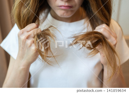 Cropped shot view of Asian woman holding her damaged split ended hair. Hair damage is risk for further damage and breakage. It may also look dull or frizzy and be difficult to manage. 141859634