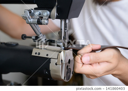 A Japanese man in his 30s sewing leather with an industrial sewing machine. A Japanese man in his 30s sewing leather with an industrial sewing machine. 141860403