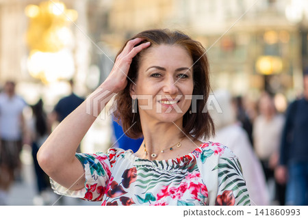 Smiling middle aged woman touching her hair on a busy city street 141860993