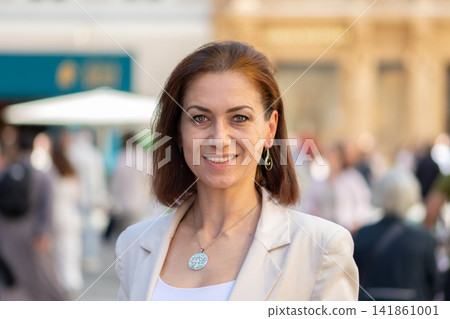 Smiling middle aged woman in beige blazer posing on busy street Smiling middle aged woman in beige blazer posing on busy street 141861001