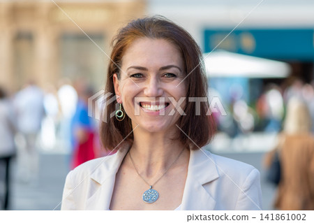 Smiling middle aged woman looking at camera in sunny city street Smiling middle aged woman looking at camera in sunny city street 141861002