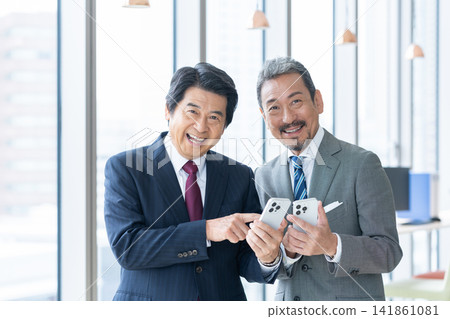 A middle-aged businessman using a smartphone in the office. Filming assistance provided by: Denpa Gakuen Educational Foundation, Tokyo Electronics College. A middle-aged businessman using a smartphone in the office. Filming assistance provided by: Denpa Gakuen Educational Foundation, Tokyo Electronics College. 141861081