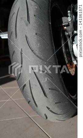 Closeup Motorcycle Rear Tire On Aluminium Swingarm And Chain, Parked In Gritty Garage, Mechanic Prepping Bike Closeup Motorcycle Rear Tire On Aluminium Swingarm And Chain, Parked In Gritty Garage, Mechanic Prepping Bike 141861871