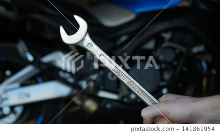 Closeup Hands Holding Wrench, Motorcycle Engine, Gritty Roadside Repair Scene With Oil Smudges, Focused Finger Closeup Hands Holding Wrench, Motorcycle Engine, Gritty Roadside Repair Scene With Oil Smudges, Focused Finger 141861954