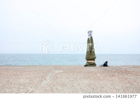 Distant monument standing on a quiet sandy beach beside calm blue sea, creating a minimalist coastal landscape with open sky, peaceful atmosphere and generous copy space for design Distant monument standing on a quiet sandy beach beside calm blue sea, creating a minimalist coastal landscape with open sky, peaceful atmosphere and generous copy space for design 141861977