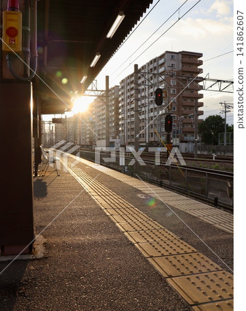 A local railway scene: a station platform and tracks illuminated by the early morning sun. Vertical composition | Vertical stock image for travel/tourism PR and social media. A local railway scene: a station platform and tracks illuminated by the early morning sun. Vertical composition | Vertical stock image for travel/tourism PR and social media. 141862607