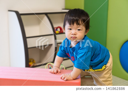 A Japanese baby boy leaning against a pink soft block in the kids' room. A Japanese baby boy leaning against a pink soft block in the kids' room. 141862886