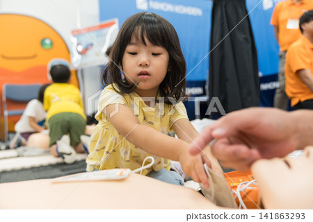 A young Japanese girl touches an AED at an emergency life-saving experience event. A young Japanese girl touches an AED at an emergency life-saving experience event. 141863293