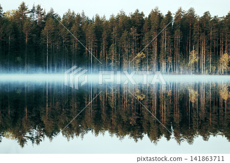 Rich range of colors of autumn forest on shore of quiet foggy lake 141863711