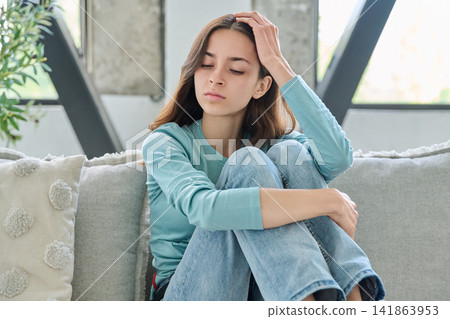 Sad young woman sitting on couch feeling anxious and lonely Sad young woman sitting on couch feeling anxious and lonely 141863953