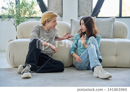 Young student friends sitting on living room floor having conversation Young student friends sitting on living room floor having conversation 141863960