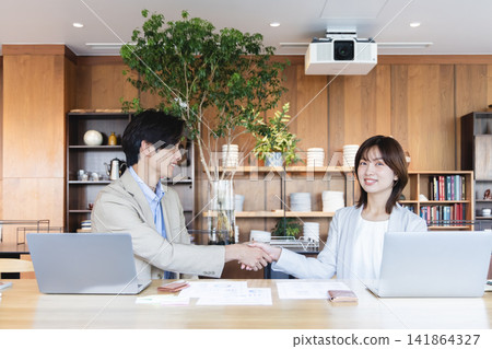 商務人士面帶微笑,握手致意,同時在辦公室打開筆記型電腦。 商務人士面帶微笑,握手致意,同時在辦公室打開筆記型電腦。 141864327