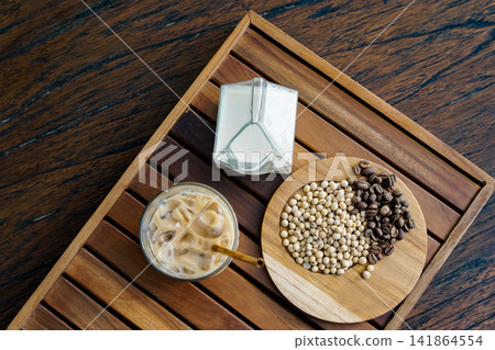 Flat Lay of Coffee Beans, Soybeans, Soy Milk, and Iced Latte on Wooden Tray for Plant Based Beverage and Cafe Lifestyle Concept Flat Lay of Coffee Beans, Soybeans, Soy Milk, and Iced Latte on Wooden Tray for Plant Based Beverage and Cafe Lifestyle Concept 141864554