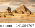 The majestic Sphinx sits before the pyramids in the Giza desert during a dramatic Egyptian sunset 141864707