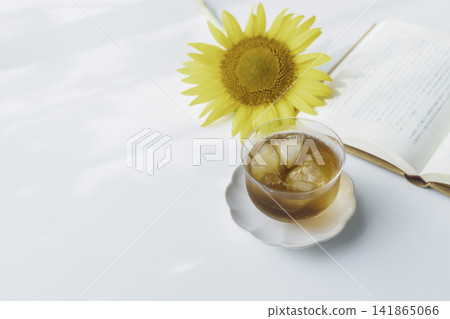 A cold cup of barley tea accompanied by sunflowers and a book – a relaxing summer moment. A cold cup of barley tea accompanied by sunflowers and a book – a relaxing summer moment. 141865066