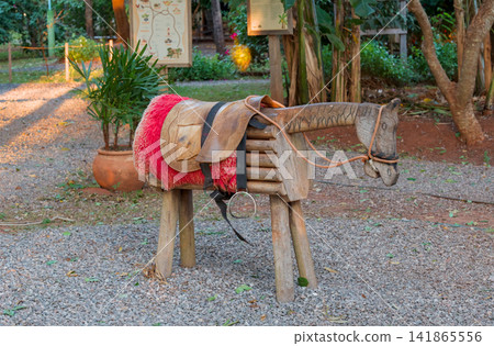A simple wooden horse with a saddle and riding equipment. A simple wooden horse with a saddle and riding equipment. 141865556