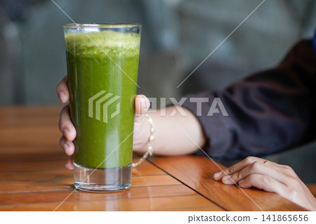 Hand Holding Green Detox Juice on Wooden Table Hand Holding Green Detox Juice on Wooden Table 141865656