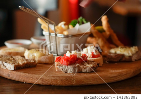 Rustic bruschetta with fresh tomatoes and cheese served on wooden board with assorted appetizers and fries in warm restaurant lighting Rustic bruschetta with fresh tomatoes and cheese served on wooden board with assorted appetizers and fries in warm restaurant lighting 141865892