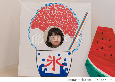 A young Japanese girl poses her face through a shaved ice-themed photo panel. A young Japanese girl poses her face through a shaved ice-themed photo panel. 141866222