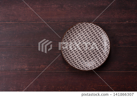 An empty round ceramic plate on a dark, textured brown background. An empty round plate An empty round ceramic plate on a dark, textured brown background. An empty round plate 141866307