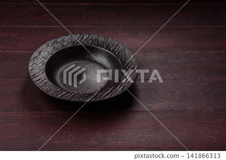 An empty round ceramic plate on a dark, textured brown background. An empty round plate An empty round ceramic plate on a dark, textured brown background. An empty round plate 141866313