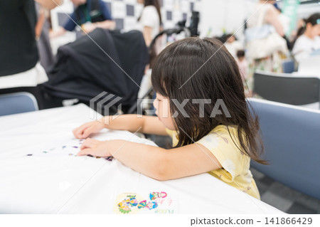 A young Japanese girl concentrates on a craft project using stickers at a workshop. A young Japanese girl concentrates on a craft project using stickers at a workshop. 141866429