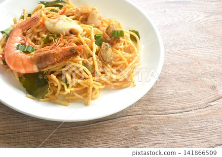 spicy stir fried spaghetti seafood slice squid and shrimp couple clam with chili and basil leaf in Thai tom yum sauce on plate  141866509